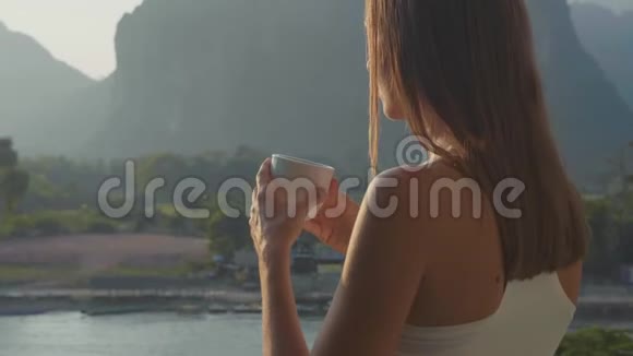 年轻女子在阳台上喝着热咖啡美丽的山景视频的预览图