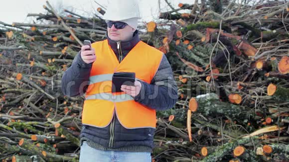 森林工程师在成堆的原木附近有平板电脑和手机视频的预览图