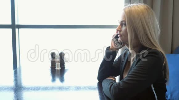 年轻的女商人西装革履地坐在咖啡馆的桌子旁用手机说话视频的预览图