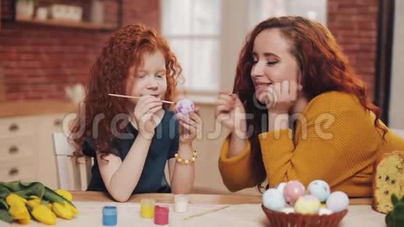 一位母亲和她的女儿在舒适的厨房里画复活节彩蛋他们笑着玩得很开心幸福的家庭准备视频的预览图
