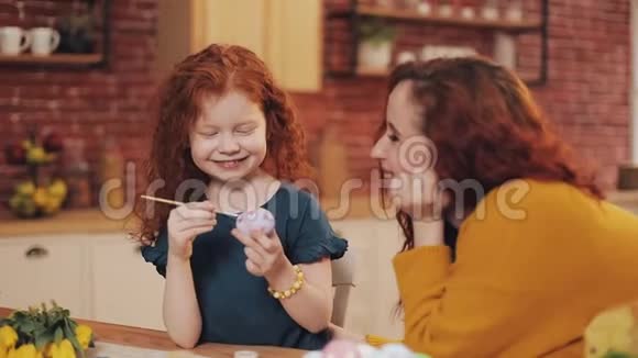 一位母亲和她的女儿在舒适的厨房里画复活节彩蛋他们笑着玩得很开心幸福的家庭准备视频的预览图