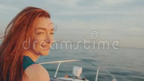 快乐的红发女孩穿着绿松石服装驾驶摩托艇美丽的日落视频的预览图
