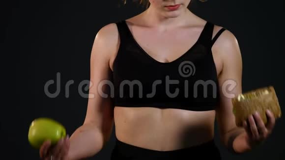 一个快乐的胖女人在汉堡或苹果之间选择的肖像被孤立在黑色的背景上视频的预览图