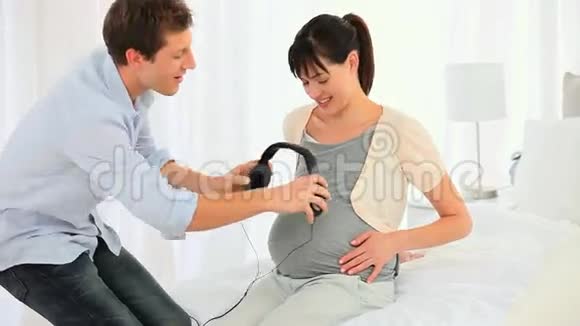 在怀孕的妻子肚子上戴耳机的男人视频的预览图