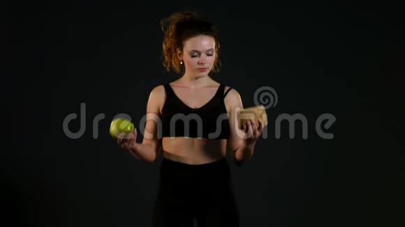 一个快乐的胖女人在汉堡或苹果之间选择的肖像被孤立在黑色的背景上视频的预览图
