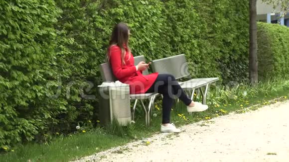 穿着红色裙子带着电话的女孩在公园的街上视频的预览图