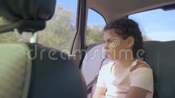 伤心的女孩无聊地坐在车里后座旅行小女孩无聊地开动汽车概念长途旅行视频的预览图