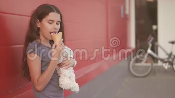 小女孩在街上吃冰淇淋有一个软玩具动作慢动作视频女孩和冰淇淋的饮食概念视频的预览图