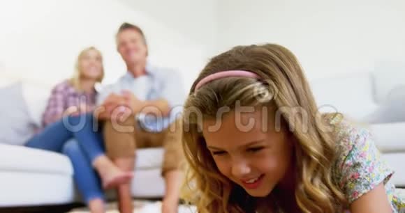 女儿在客厅里使用数码平板电脑而父母则坐在沙发上视频的预览图