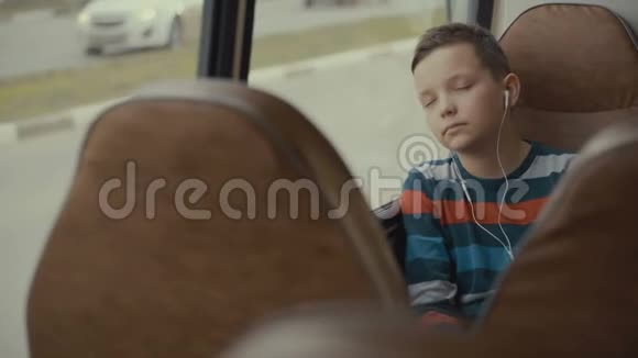 一个小男孩乘公共汽车穿过城市的特写镜头他听音乐视频的预览图