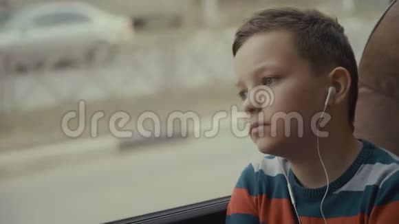 一个小男孩乘公共汽车穿过城市的特写镜头他听音乐视频的预览图