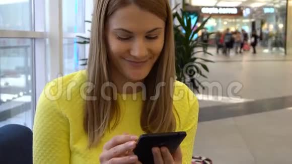 年轻漂亮的女人在商场里带着智能手机浏览互联网与朋友交流视频的预览图
