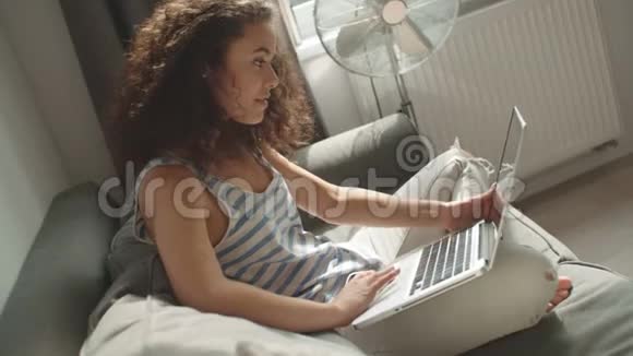漂亮的女人在客厅里用笔记本电脑在沙发上放松视频的预览图