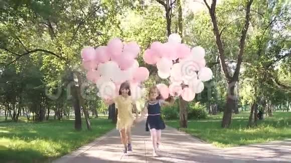 孩子们拿着一大堆五颜六色的气球穿过公园两个带气球的小女孩视频的预览图