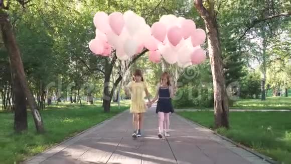 孩子们拿着一大堆五颜六色的气球穿过公园两个带气球的小女孩视频的预览图