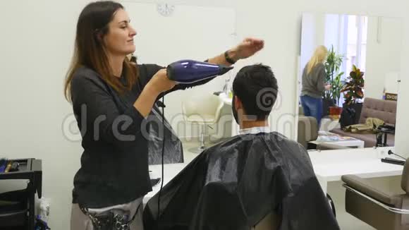 专业美发店烘干头发男青年顾客和女理发师视频的预览图