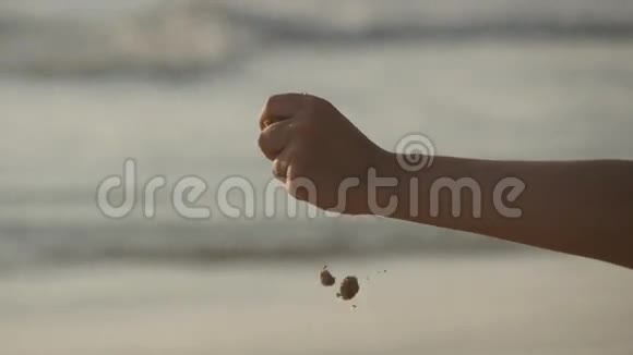 日落时分在海洋背景下女性用手在手指上撒着海沙带沙子的年轻女子手臂视频的预览图