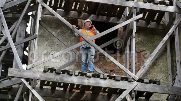 建筑工人站在木脚手架上用智能手机说话视频的预览图