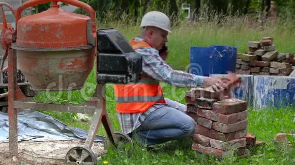 建筑工人在混凝土搅拌机附近检查旧砖和智能电话视频的预览图