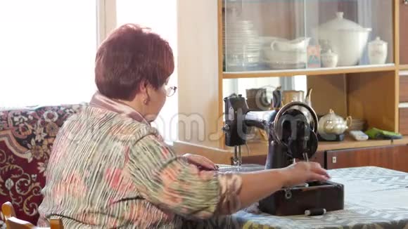 成年妇女在旧的手工缝纫机上缝纫眼镜穿着灰色布缝上视频的预览图