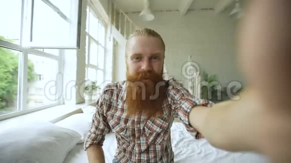 一个长胡子的年轻人用平板电脑在家里坐在床上聊天视频的预览图