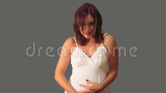 美丽的孕妇抱着她的腹部微笑视频的预览图