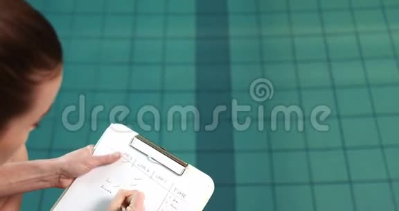 女教练在泳池边写笔记视频的预览图