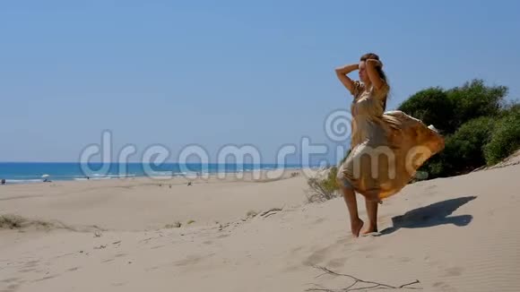 年轻漂亮的女人穿着金色的长裙站在靠近大海的沙丘上视频的预览图