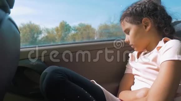 伤心的女孩无聊地坐在车后座上运动旅行小女孩在车里无聊概念车视频的预览图