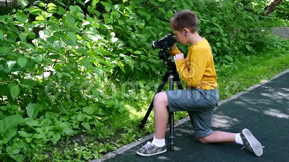 小男孩带着摄像机拍摄大自然中的绿色公园慢动作视频的预览图