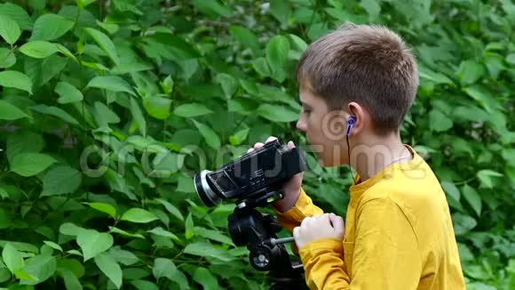 带着摄像机的小男孩在绿色公园慢动作拍摄关于自然的电影视频的预览图
