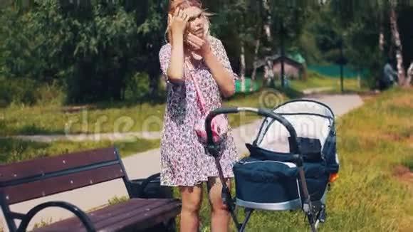妈妈带着婴儿车在夏天公园打电话阳光明媚散步视频的预览图