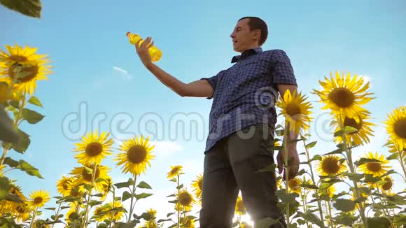 农夫穿着格子衬衫手里拿着一个塑料瓶向日葵油站在田野里慢动作视频的预览图