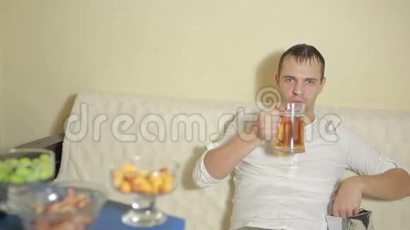 年轻人在家里的沙发上喝啤酒看电视视频的预览图