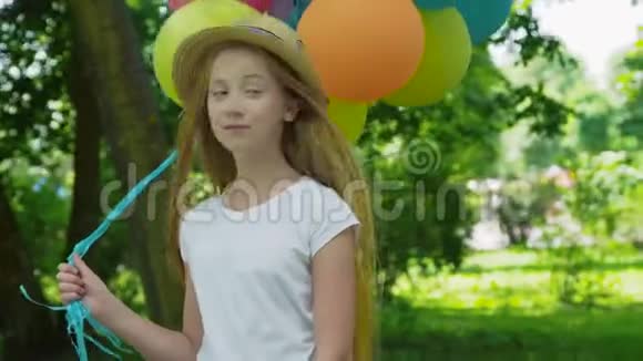 在阳光明媚的公园里美丽的女孩用五颜六色的气球在镜头前摆姿势的肖像视频的预览图