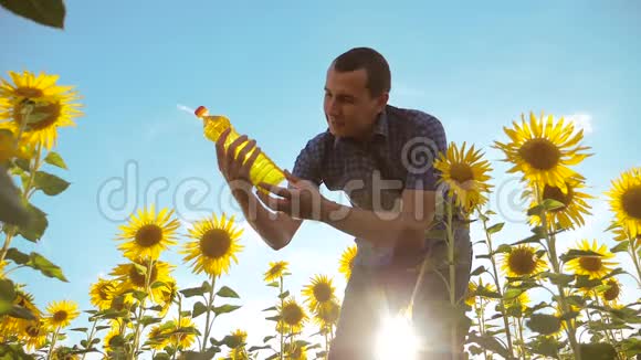 穿着格子衬衫的农夫手里拿着一个塑料瓶向日葵油站在田野里慢速视频视频的预览图