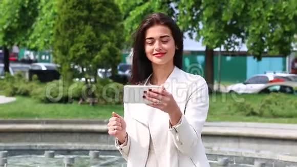 女孩用智能手机笑的肖像在喷泉背景上带着手机的漂亮年轻女人很幸福的女人视频的预览图