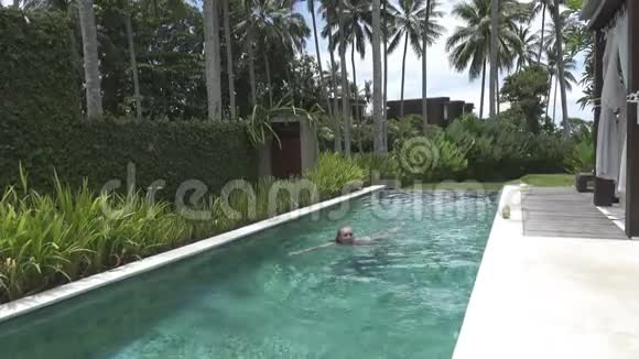 年轻苗条的女人在棕榈树下的热带度假胜地的游泳池里休息视频的预览图
