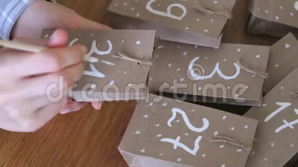 女人为孩子们制作圣诞来临日历用刷子和白色油漆在袋子上写一个数字特写双手视频的预览图