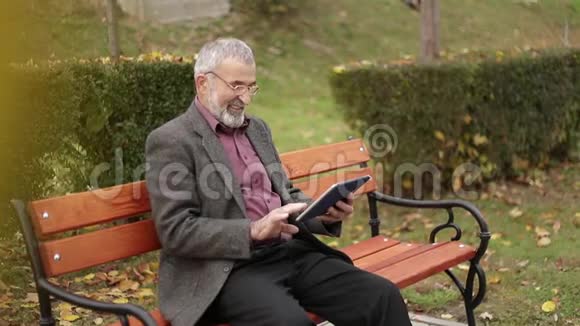 爷爷坐在公园的长凳上用平板电脑视频的预览图