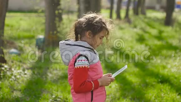 春天在森林里绿草如茵的背景下在网游中玩平板电脑的少女视频的预览图