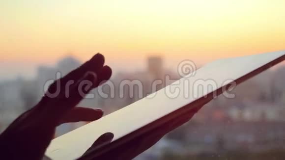 在美丽的夕阳下女商人在办公室里用平板电脑在城市上空用玻璃窗视频的预览图