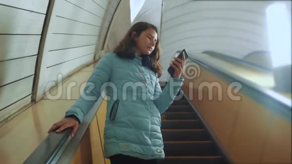 少女生活方式地下地铁乘坐自动扶梯手持智能手机小女孩黑发女儿视频的预览图