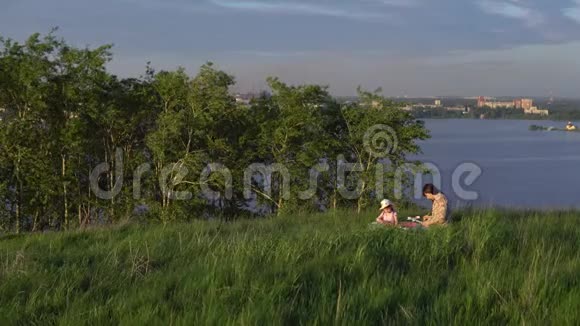 妈妈和女儿在池塘附近的山上野餐视频的预览图