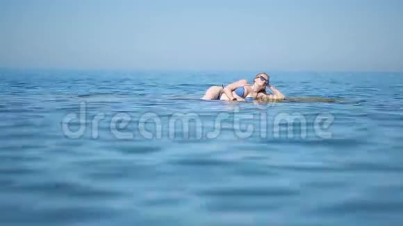 穿着蓝色比基尼的女孩在海浪中躺在海滩上玩得很开心视频的预览图