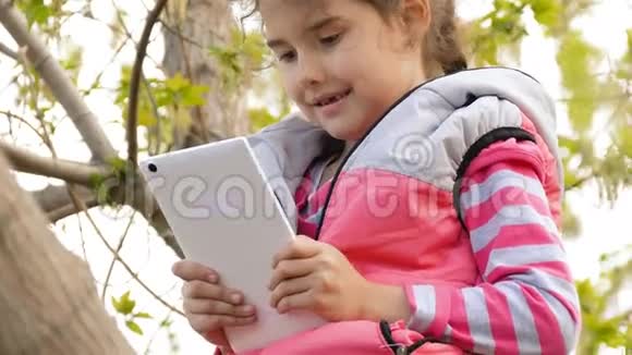 少女在线游戏玩平板电脑坐在树上视频的预览图