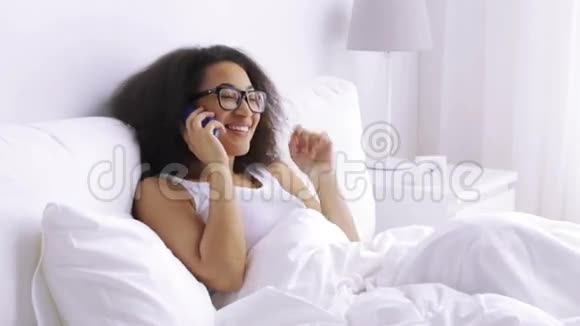 非洲女人在家里的床上打电话给智能手机视频的预览图