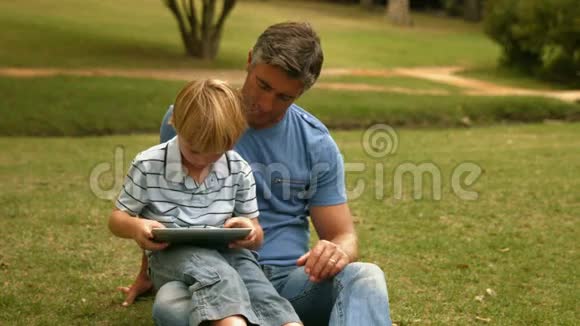 快乐的父亲和儿子在公园里用平板电脑视频的预览图