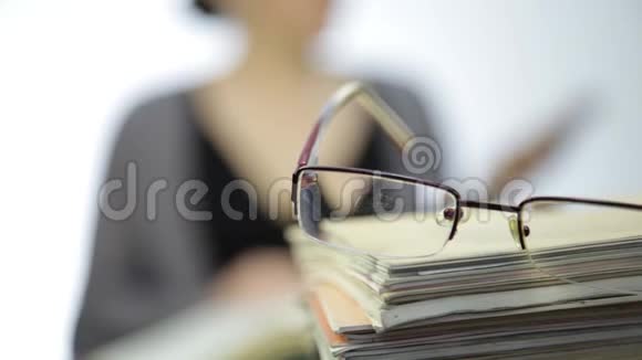 一堆练习册上的眼镜和背景模糊的商务女性视频的预览图