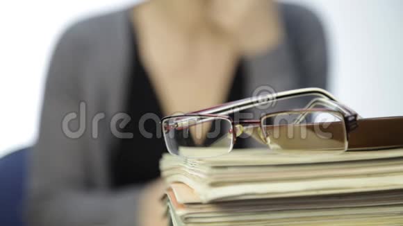 一堆练习册上的眼镜和背景模糊的商务女性视频的预览图